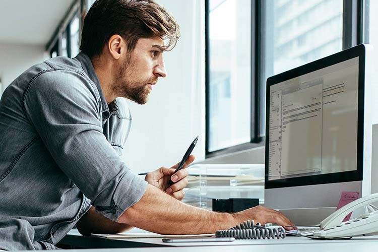 デスクに座ってコンピュータで作業している男性。 
